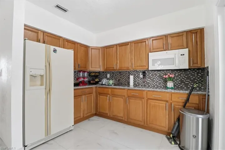 Kitchen with brown cabinets, white appliances, light stone counters, and light marble finish floors