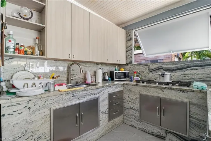 Kitchen featuring open shelves, light stone countertops, appliances with stainless steel finishes, and tasteful backsplash