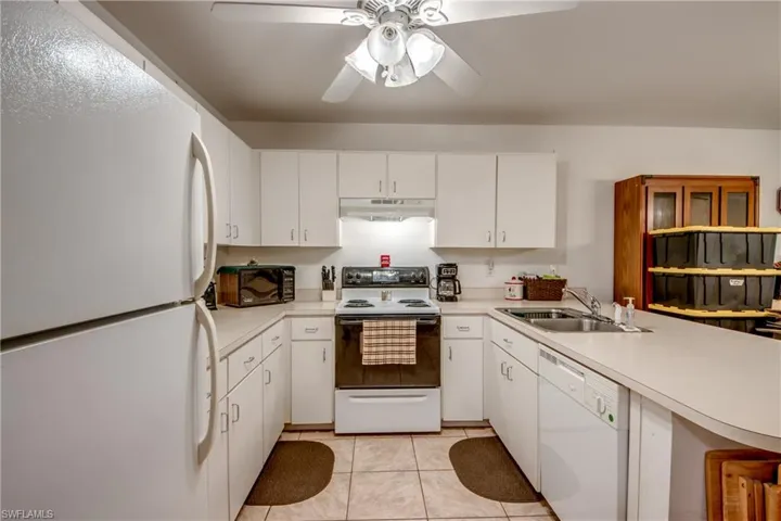 Kitchen featuring white cabinets, white appliances, sink, light tile patterned floors, and ceiling fan