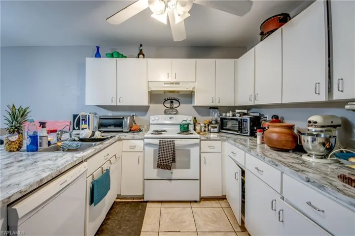 Kitchen with light tile patterned flooring, ceiling fan, white cabinets, white appliances, and sink