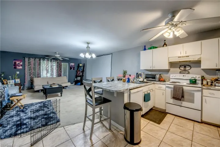 Kitchen with white cabinets, a kitchen breakfast bar, white appliances, and light tile patterned floors