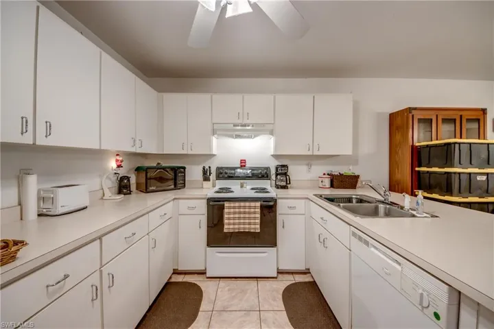 Kitchen featuring sink, ceiling fan, white appliances, and white cabinetry