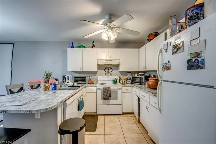Kitchen featuring white cabinetry, ceiling fan, white appliances, a kitchen bar, and light tile patterned floors