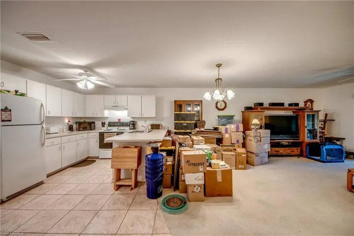Kitchen featuring white cabinetry, white appliances, ceiling fan with notable chandelier, hanging light fixtures, and light carpet