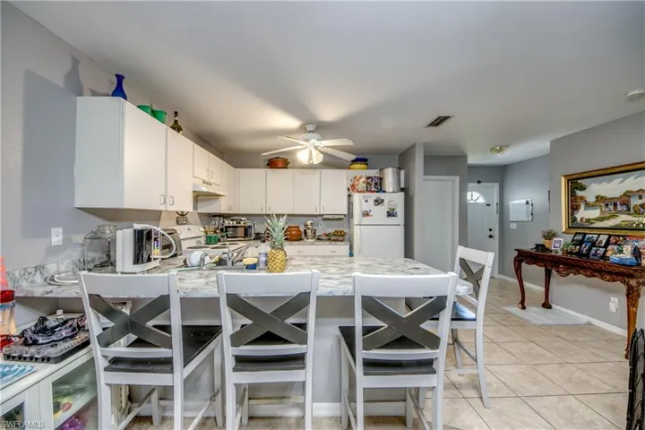 Kitchen featuring white appliances, kitchen peninsula, light tile patterned floors, white cabinetry, and ceiling fan