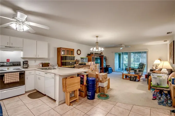 Kitchen with white cabinetry, white appliances, light colored carpet, hanging light fixtures, and sink