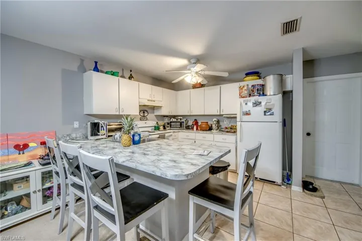Kitchen with light tile patterned flooring, white cabinetry, white appliances, kitchen peninsula, and ceiling fan