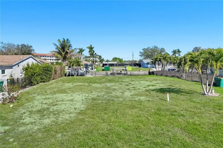 Expansive grass lot featuring mature palm trees and perimeter fencing - Virtually Edited Image