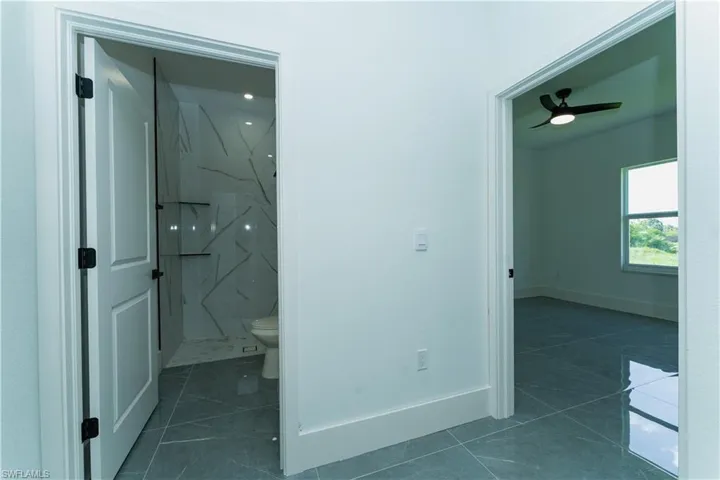 Bathroom featuring a marble finish shower, toilet, baseboards, and tile patterned flooring