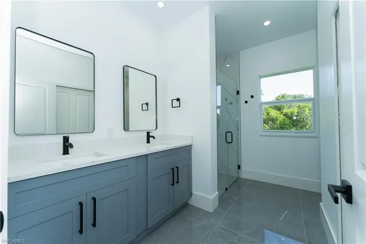 Bathroom featuring baseboards, double vanity, a shower stall, marble finish flooring, and recessed lighting
