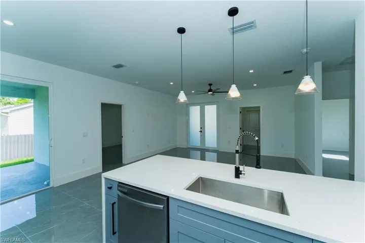 Kitchen featuring a sink, dishwasher, open floor plan, decorative light fixtures, and light stone counters