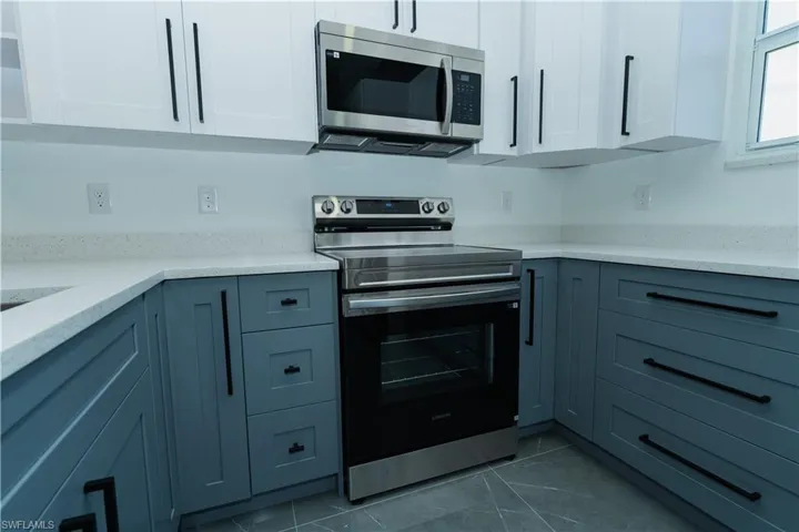 Kitchen with appliances with stainless steel finishes, white cabinetry, and light stone countertops