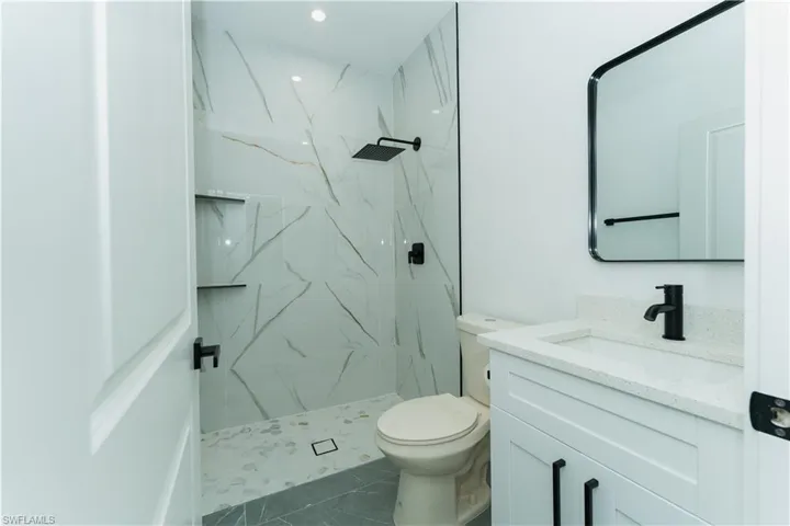 Bathroom with vanity, a marble finish shower, toilet, and recessed lighting