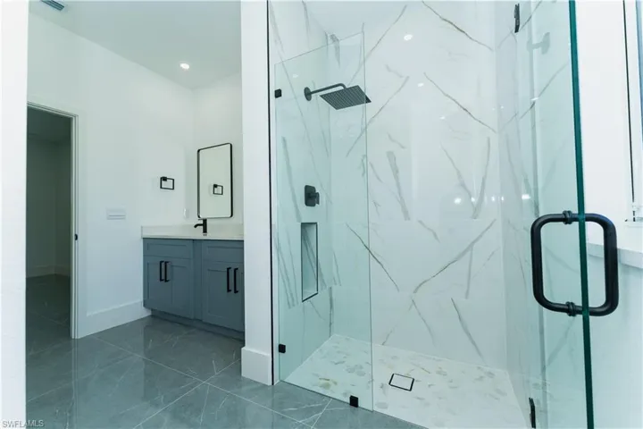 Bathroom featuring a marble finish shower, vanity, marble look tiles, baseboards, and recessed lighting