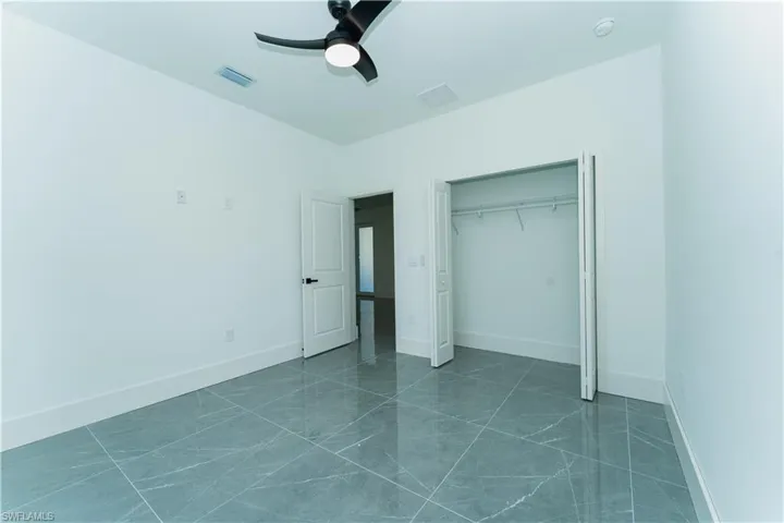 Unfurnished bedroom with a ceiling fan, a closet, baseboards, and dark marble finish floors