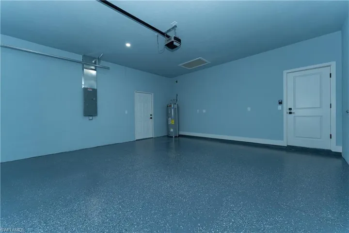 Garage featuring secured water heater, a garage door opener, electric panel, and recessed lighting