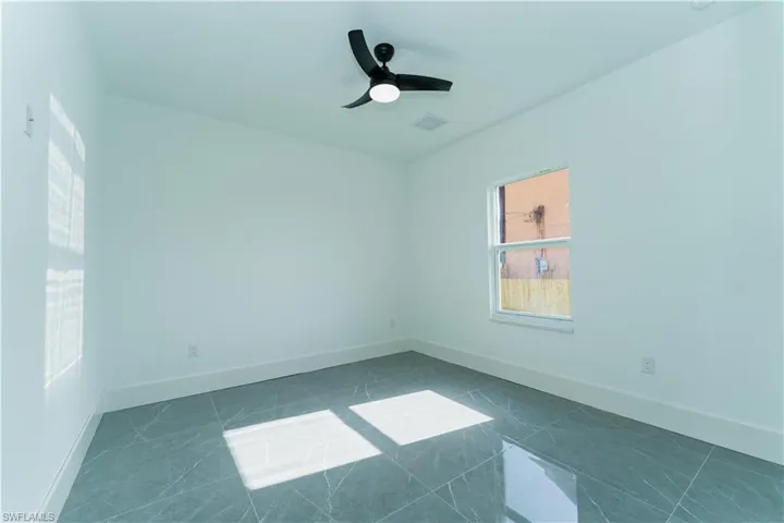 Empty room with ceiling fan, baseboards, and dark tile patterned flooring