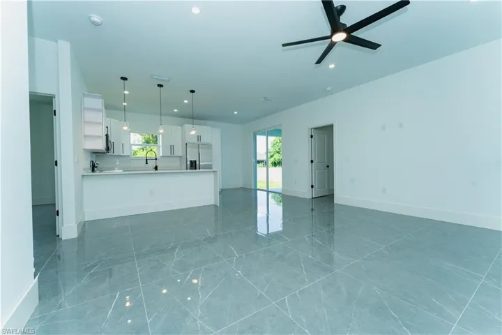 Unfurnished living room featuring a ceiling fan, recessed lighting, light marble finish flooring, baseboards, and a sink