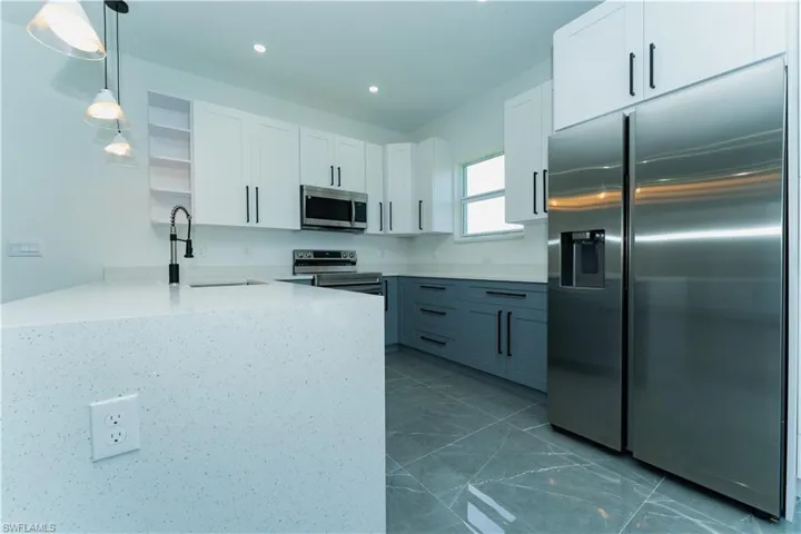 Kitchen with appliances with stainless steel finishes, a peninsula, open shelves, a sink, and white cabinetry
