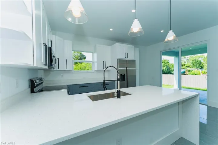 Kitchen featuring electric stove, stainless steel fridge with ice dispenser, a sink, a peninsula, and white cabinetry