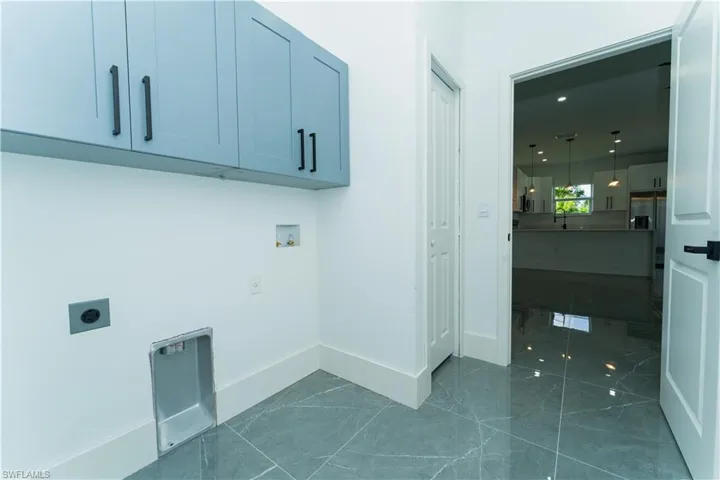 Laundry area featuring hookup for an electric dryer, hookup for a washing machine, cabinet space, baseboards, and dark marble finish flooring