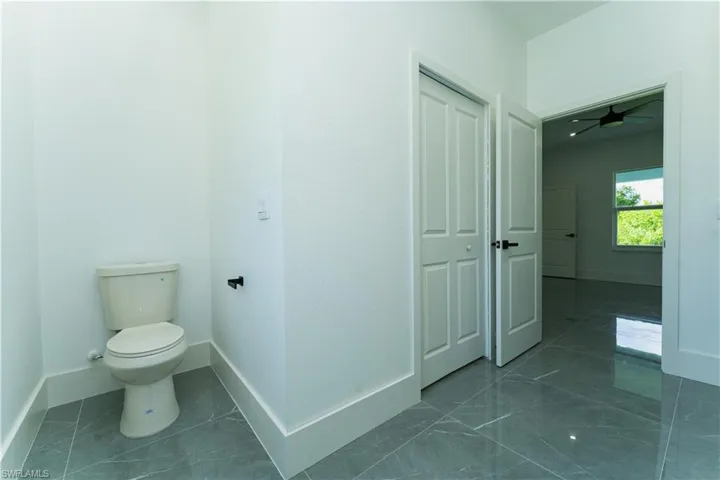 Bathroom featuring toilet, baseboards, marble look tile flooring, and ceiling fan
