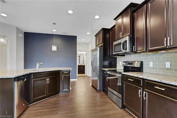 Kitchen with dark brown cabinetry, stainless steel appliances, light stone countertops, recessed lighting, and decorative light fixtures
