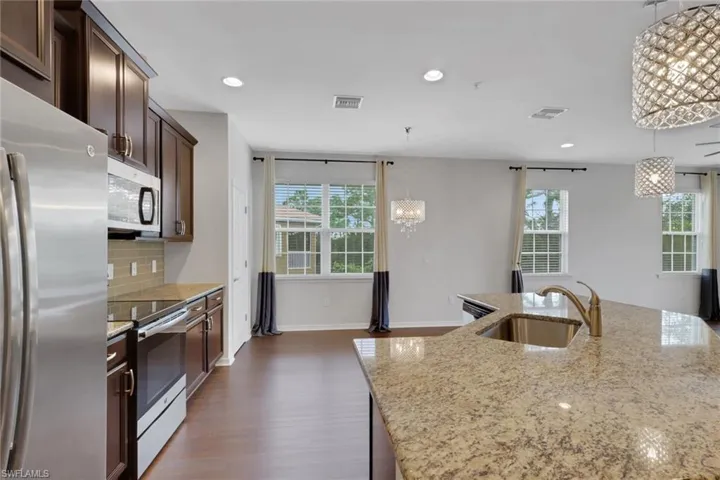 Kitchen featuring appliances with stainless steel finishes, light stone countertops, recessed lighting, a chandelier, and dark brown cabinetry