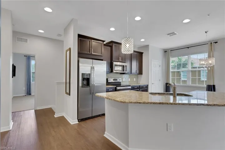 Kitchen with dark brown cabinetry, stainless steel appliances, backsplash, light stone countertops, and hanging light fixtures