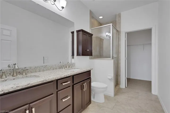 Full bath with double vanity, a shower stall, a spacious closet, and light tile patterned floors