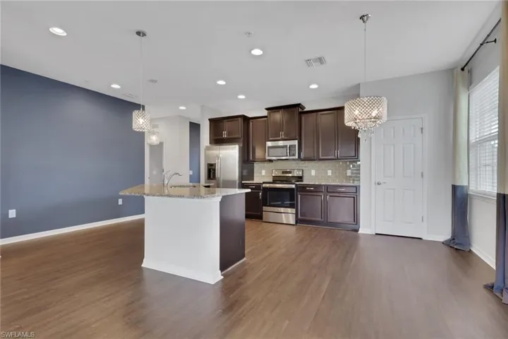 Kitchen featuring a chandelier, appliances with stainless steel finishes, dark brown cabinets, hanging light fixtures, and light stone counters