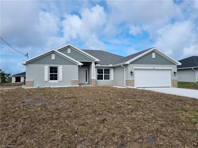 Craftsman-style home featuring stucco siding, a garage, a front lawn, and driveway