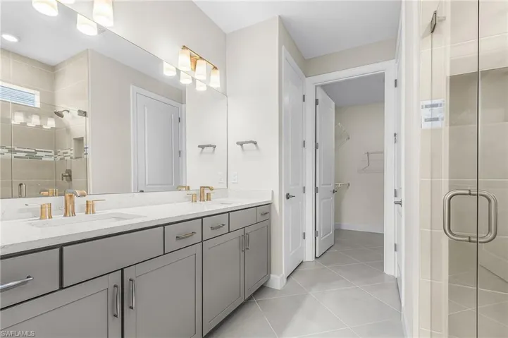 Bathroom with a shower stall, double vanity, light tile patterned floors, and a spacious closet