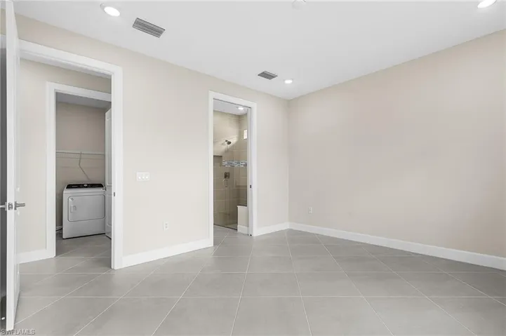 Unfurnished bedroom featuring washer / dryer, light tile patterned floors, connected bathroom, and recessed lighting