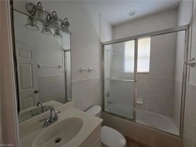 Full bathroom with toilet, vanity, shower / bath combination with glass door, and tile walls