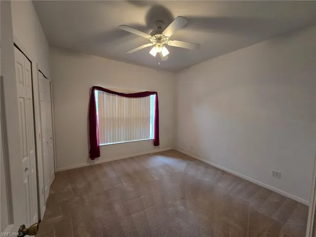 Unfurnished bedroom with ceiling fan and dark colored carpet