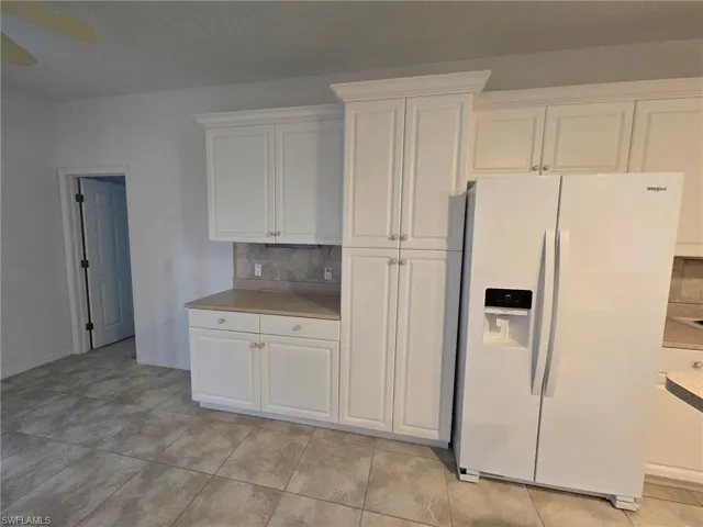 Kitchen featuring tasteful backsplash, white refrigerator with ice dispenser, and white cabinets