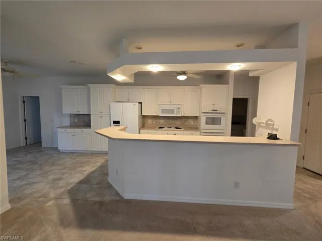 Kitchen featuring a kitchen island, white cabinetry, decorative backsplash, ceiling fan, and white appliances