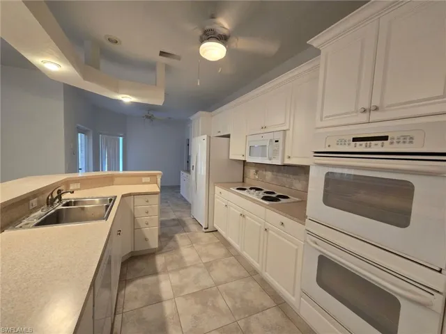 Kitchen featuring tasteful backsplash, sink, white cabinets, and white appliances