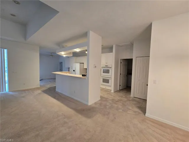 Kitchen featuring white cabinetry, white appliances, kitchen peninsula, and light colored carpet