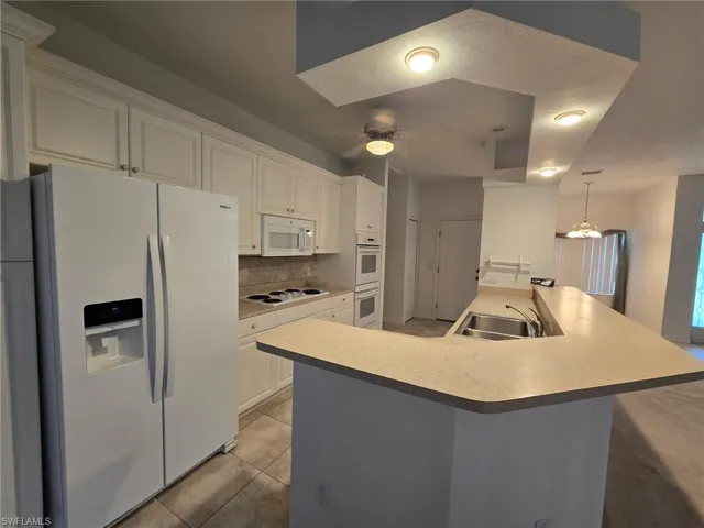 Kitchen with tasteful backsplash, white cabinetry, an island with sink, sink, and white appliances