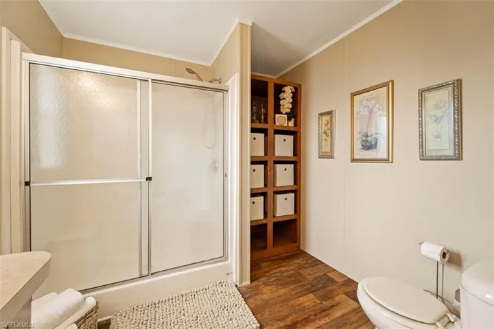 Bathroom with walk in shower, ornamental molding, toilet, and wood-type flooring
