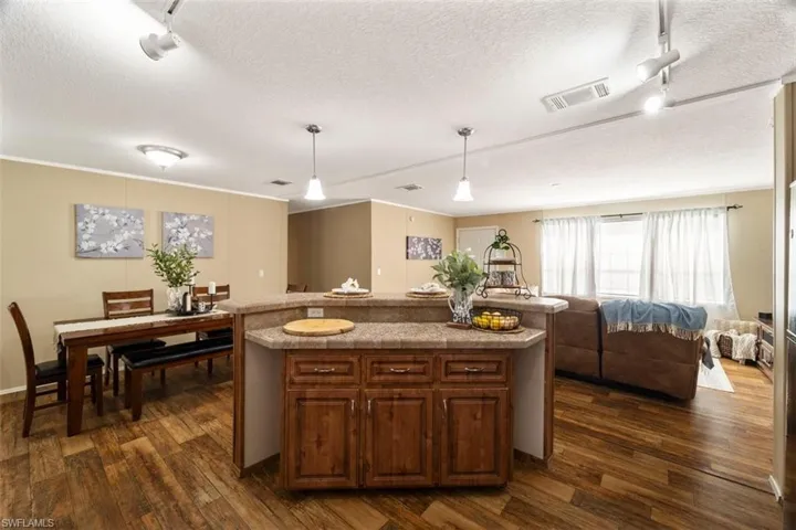 Kitchen with dark hardwood / wood-style floors, a center island with sink, rail lighting, a textured ceiling, and pendant lighting