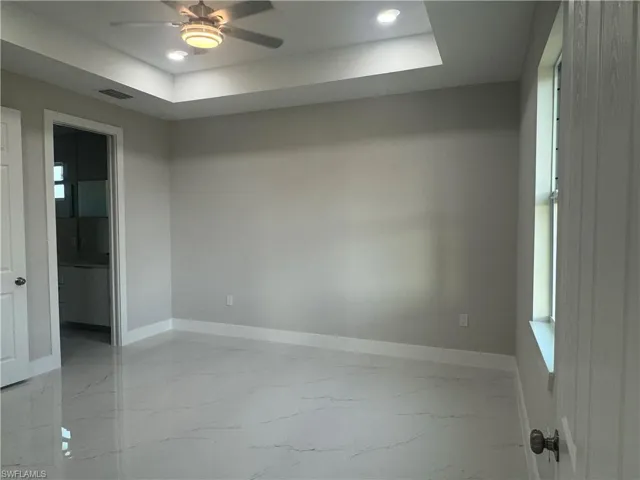 Tiled empty room with ceiling fan and a raised ceiling