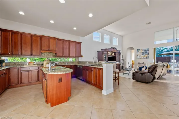 Kitchen with light stone countertops, light tile patterned floors, a kitchen bar, and a center island with sink