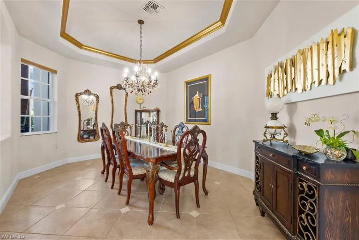 Tiled dining room with a tray ceiling, an inviting chandelier, and ornamental molding