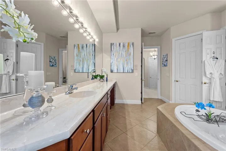 Bathroom with tile patterned floors, tiled bath, vanity, and a notable chandelier