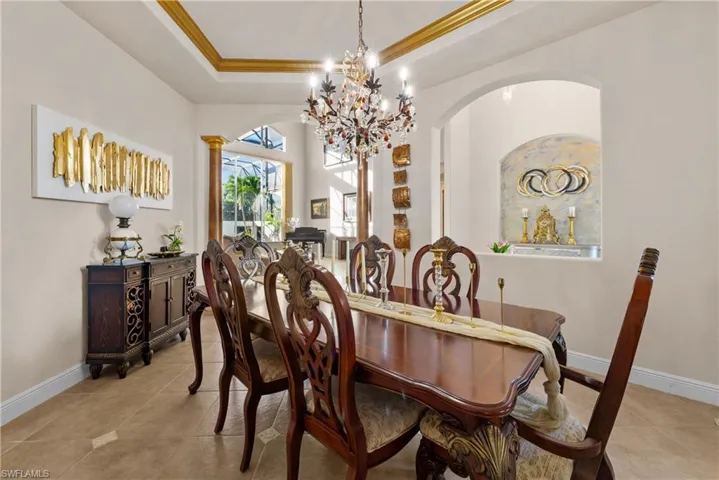 Dining area featuring a raised ceiling, a notable chandelier, decorative columns, light tile patterned floors, and ornamental molding