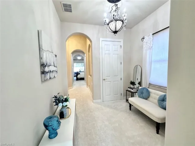 Hall featuring light carpet and a notable chandelier