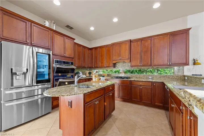 Kitchen featuring light stone counters, a kitchen island with sink, sink, and appliances with stainless steel finishes